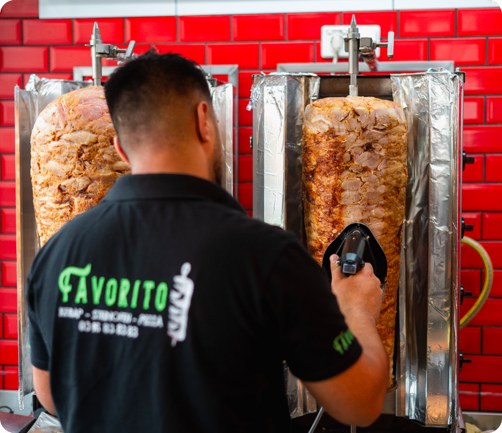 Koch schneidet Döner-Kebabfleisch am Drehspieß vor roter Wand in der Küche von Favorito Graz